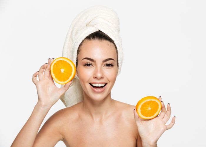 Frau mit Handtuch auf dem Kopf hält frische Orangenscheiben als Symbolbild für Hautpflege.