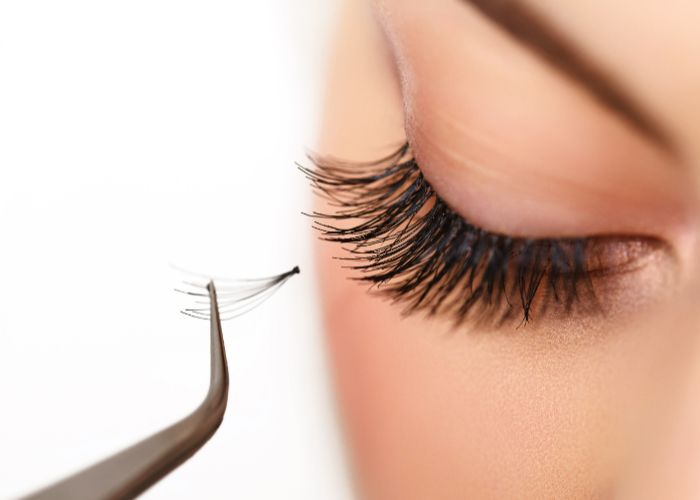 Präzises Anbringen künstlicher Wimpern mit einer Pinzette in Nahaufnahme.