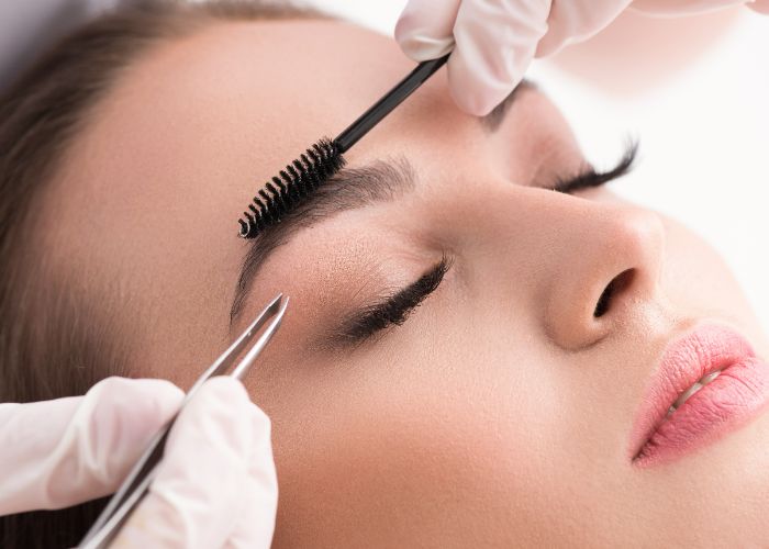 Präzise Augenbrauenkorrektur mit Pinzette während einer kosmetischen Behandlung.
