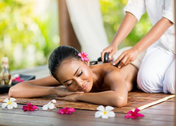 Frau erhält eine entspannende Rückenmassage mit Blumenarrangement im Hintergrund.